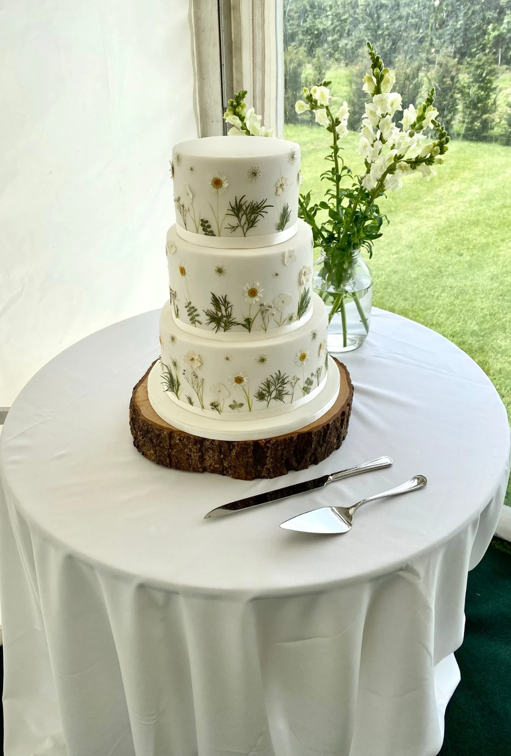 Three-tier white cake with painted green foliage on a log slice