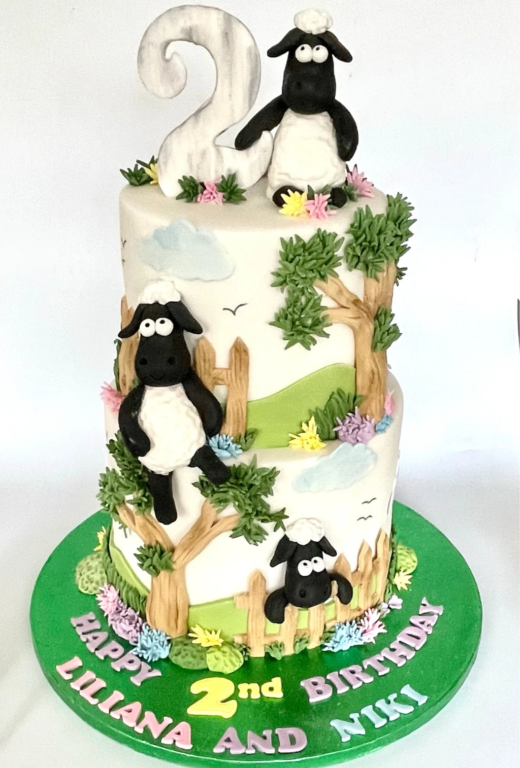 Two-tier countryside cake with sheep figures, trees, flowers and a number two topper