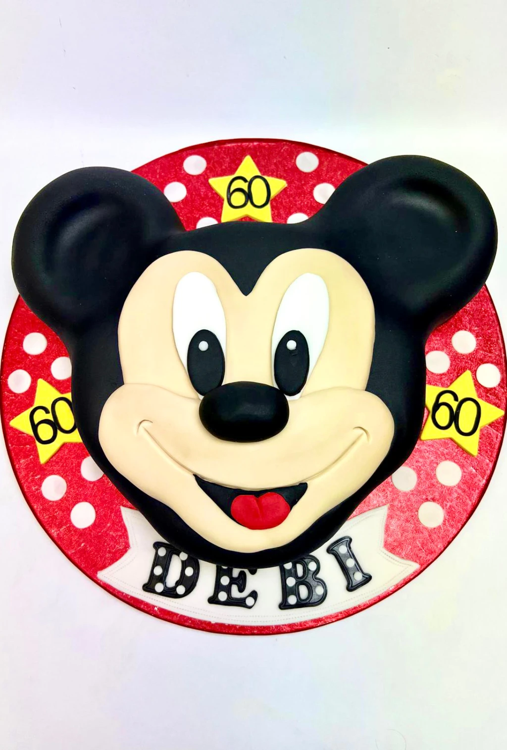 Mickey Mouse face cake on a red polka-dot board with 60th birthday stars