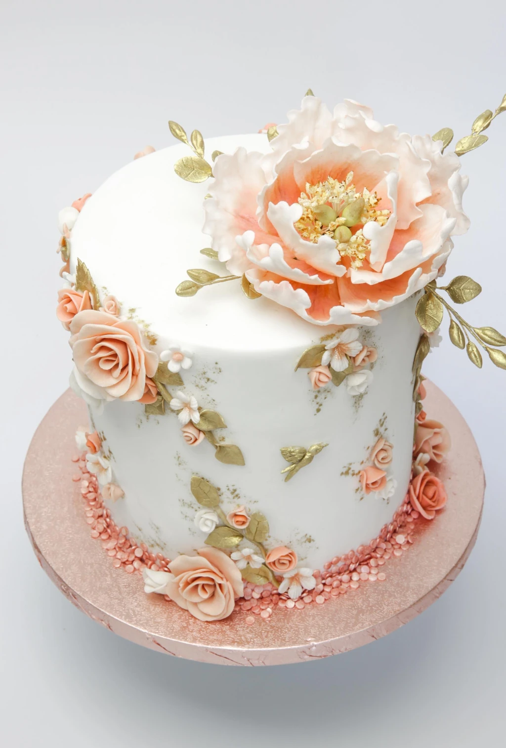 White cake with a large peach flower, small roses and gold leaves