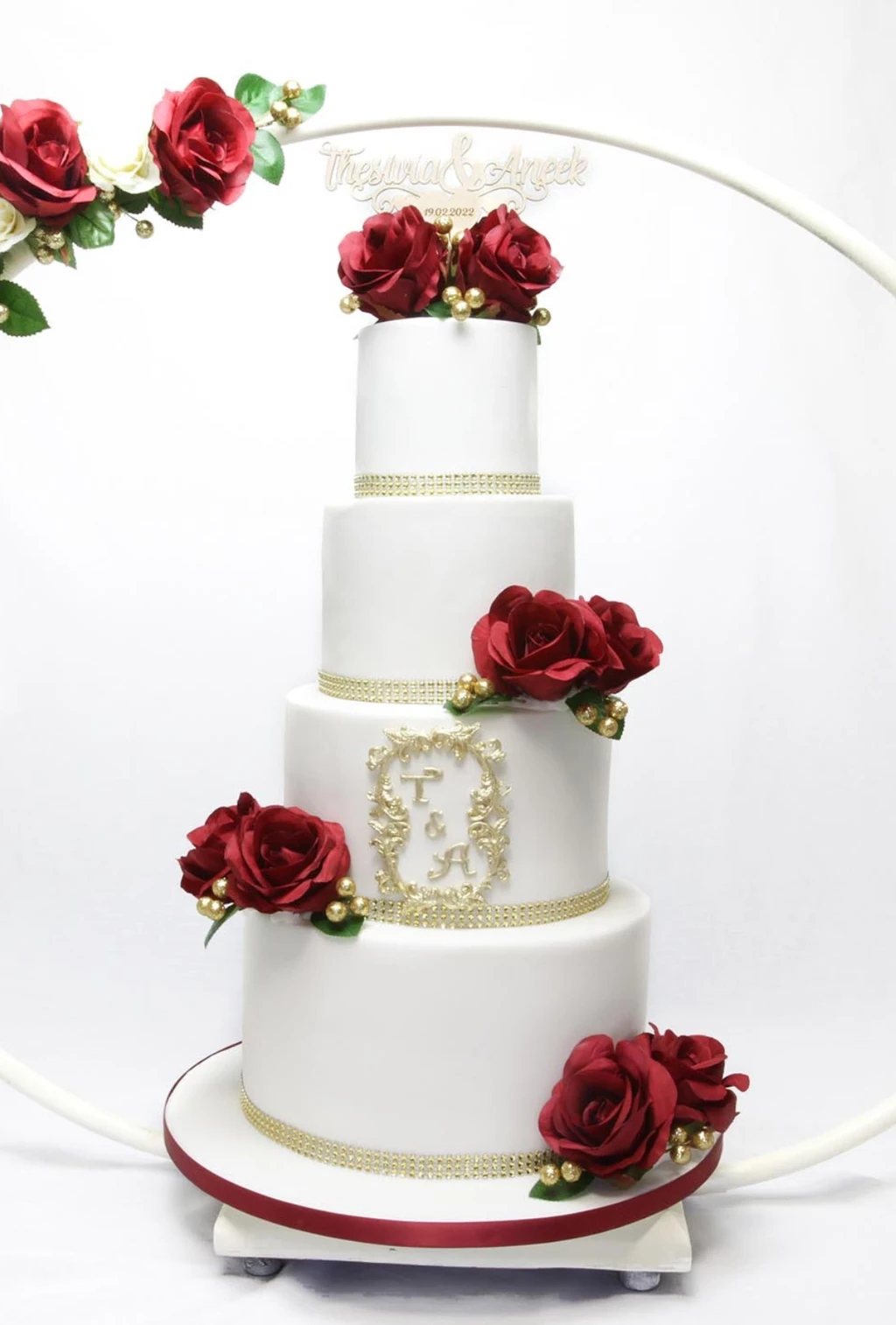 Four-tier white cake with red roses and gold monogram detailing