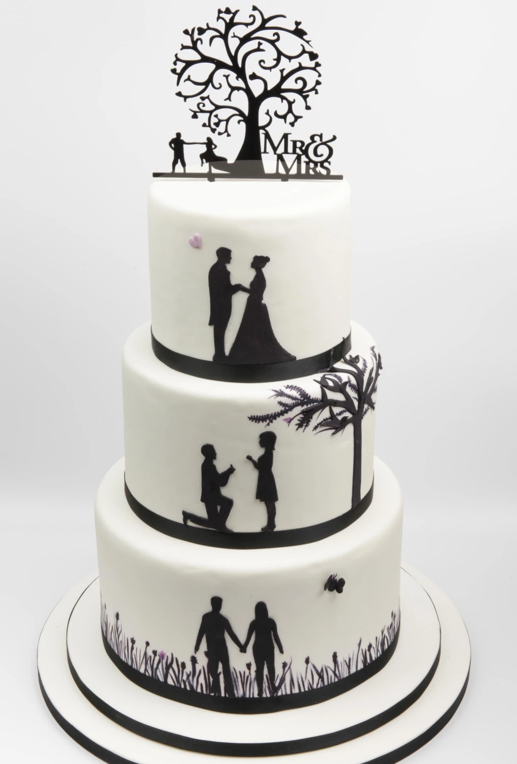 Three-tier white cake with black family silhouettes and a tree topper