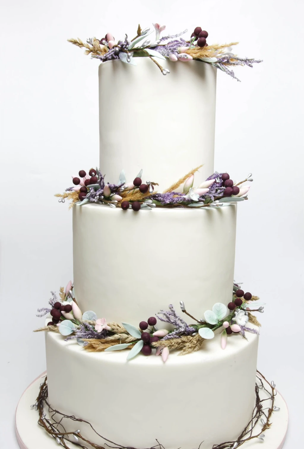 Three-tier white cake with branches, berries and foliage between the tiers