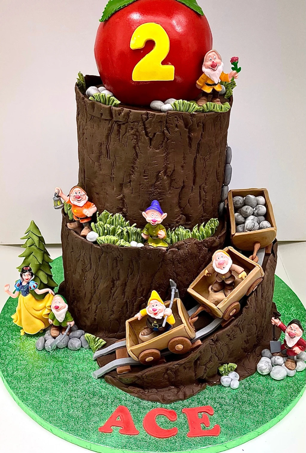 Woodland-themed second birthday cake with Snow White, dwarf figures, mine carts and a large red apple