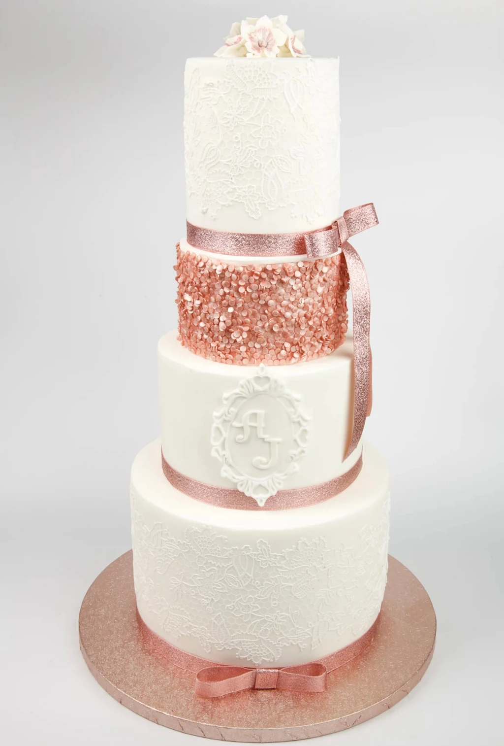 Four-tier white cake with a rose-gold glitter tier and pink ribbons