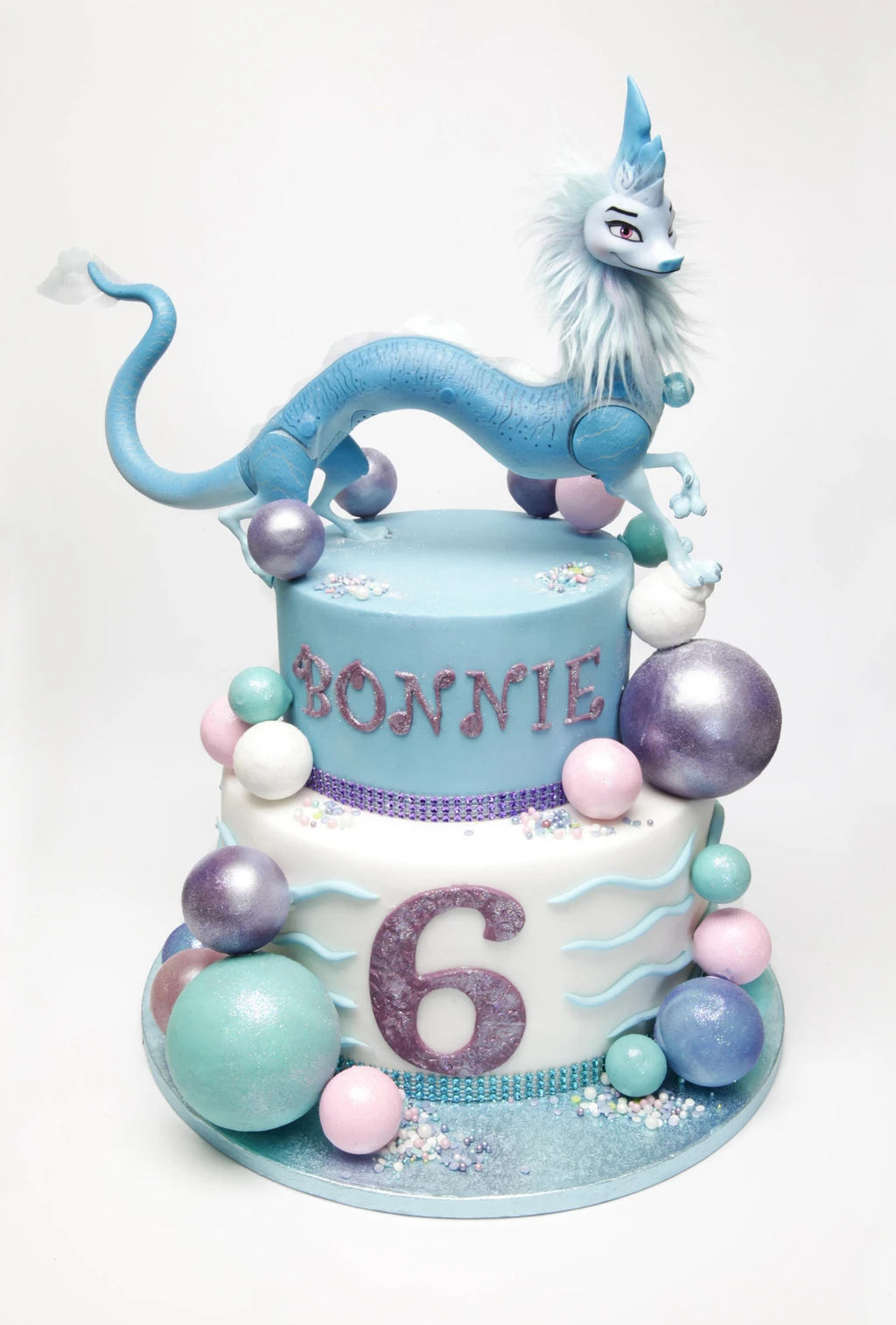Blue and white sixth birthday cake with a blue dragon figure and pastel spheres