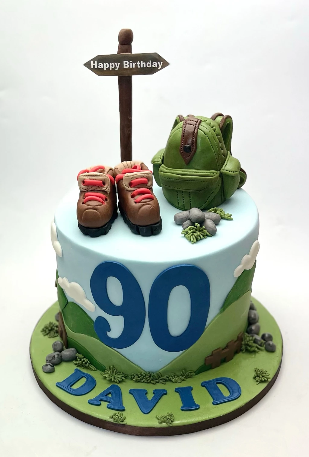 Walking-themed 90th birthday cake with boots, a green rucksack and a signpost