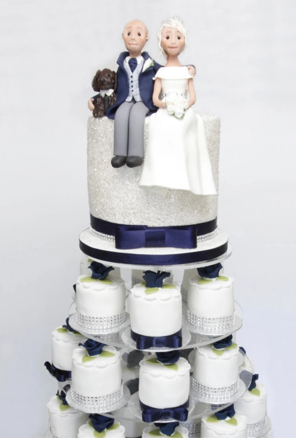 White wedding cake with bride and groom figures above a stand of cupcakes