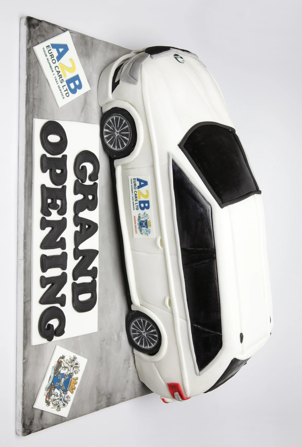 Sculpted white car cake on a road-effect board with a grand opening sign