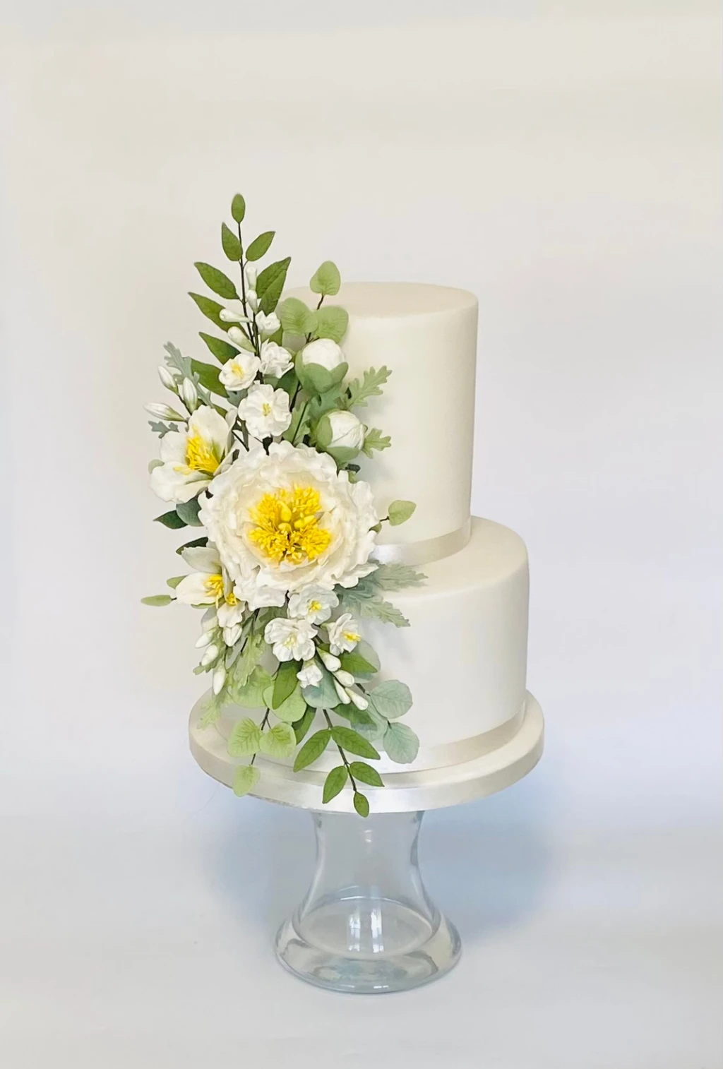 Two-tier white cake with yellow and white flowers and green leaves