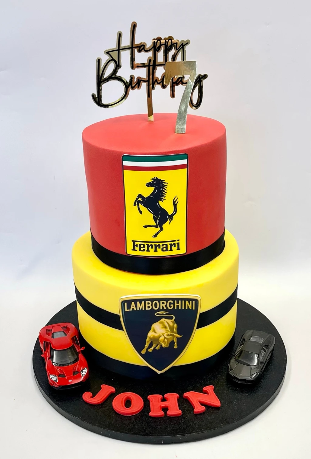 Red and yellow two-tier seventh birthday cake with Ferrari and Lamborghini emblems and model cars