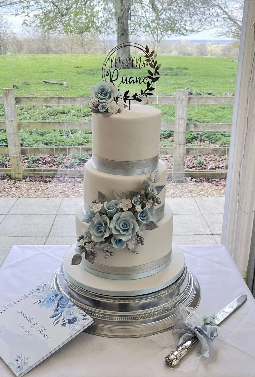 Three-tier white cake with pale blue roses and a circular topper