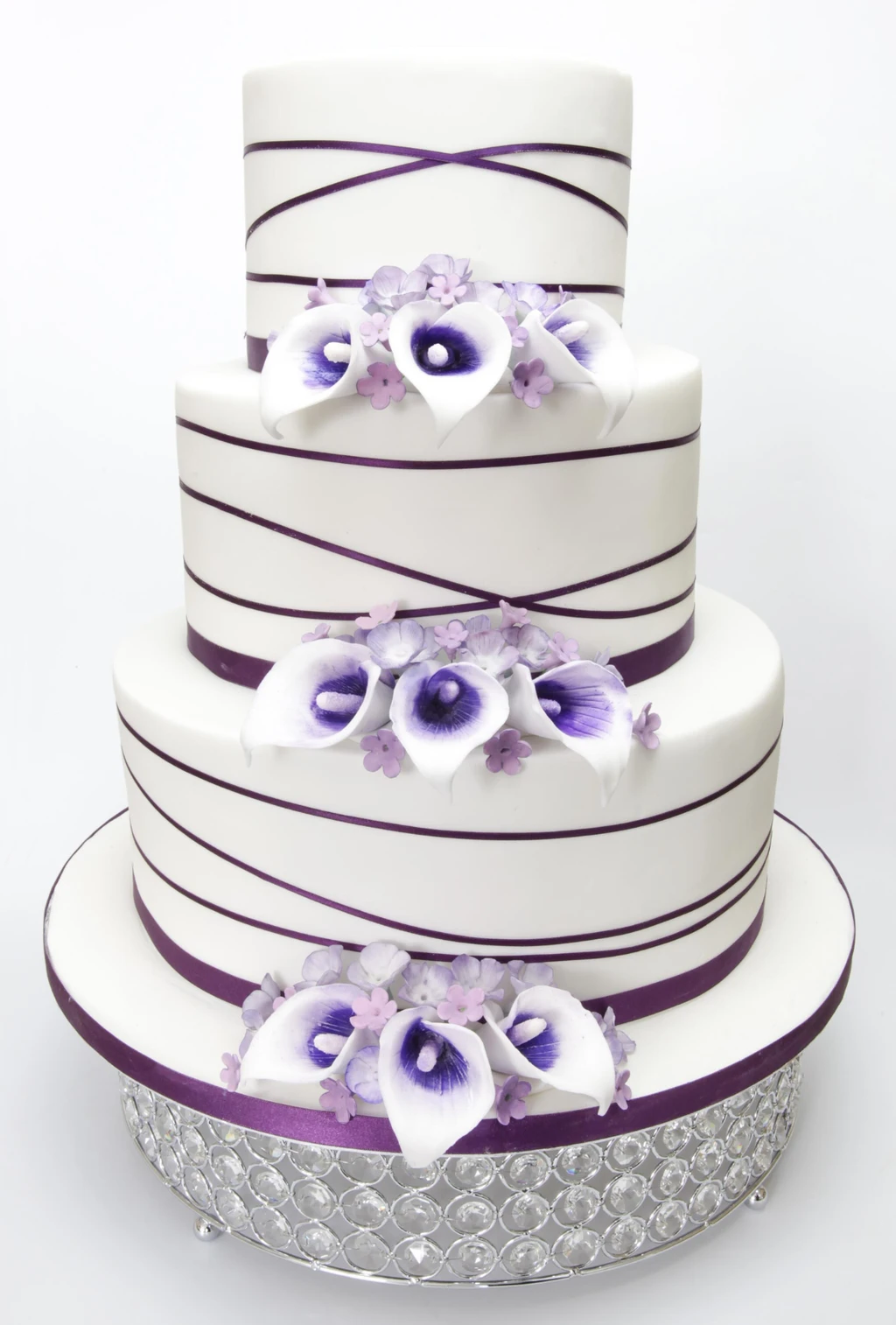 Three-tier white cake with purple ribbons and purple and white flowers