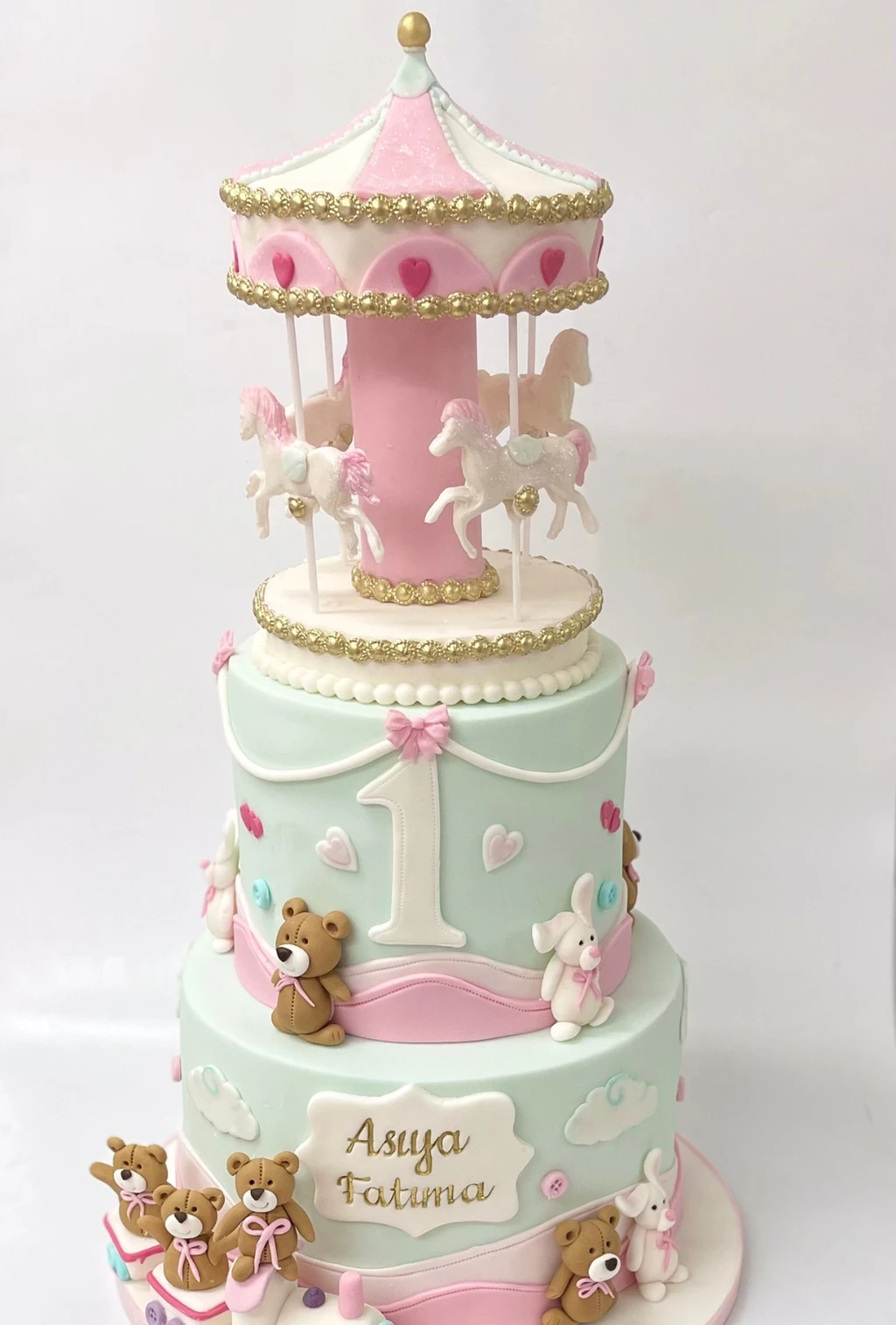 Pastel first birthday cake with a pink carousel, teddy bears, rabbits and bows