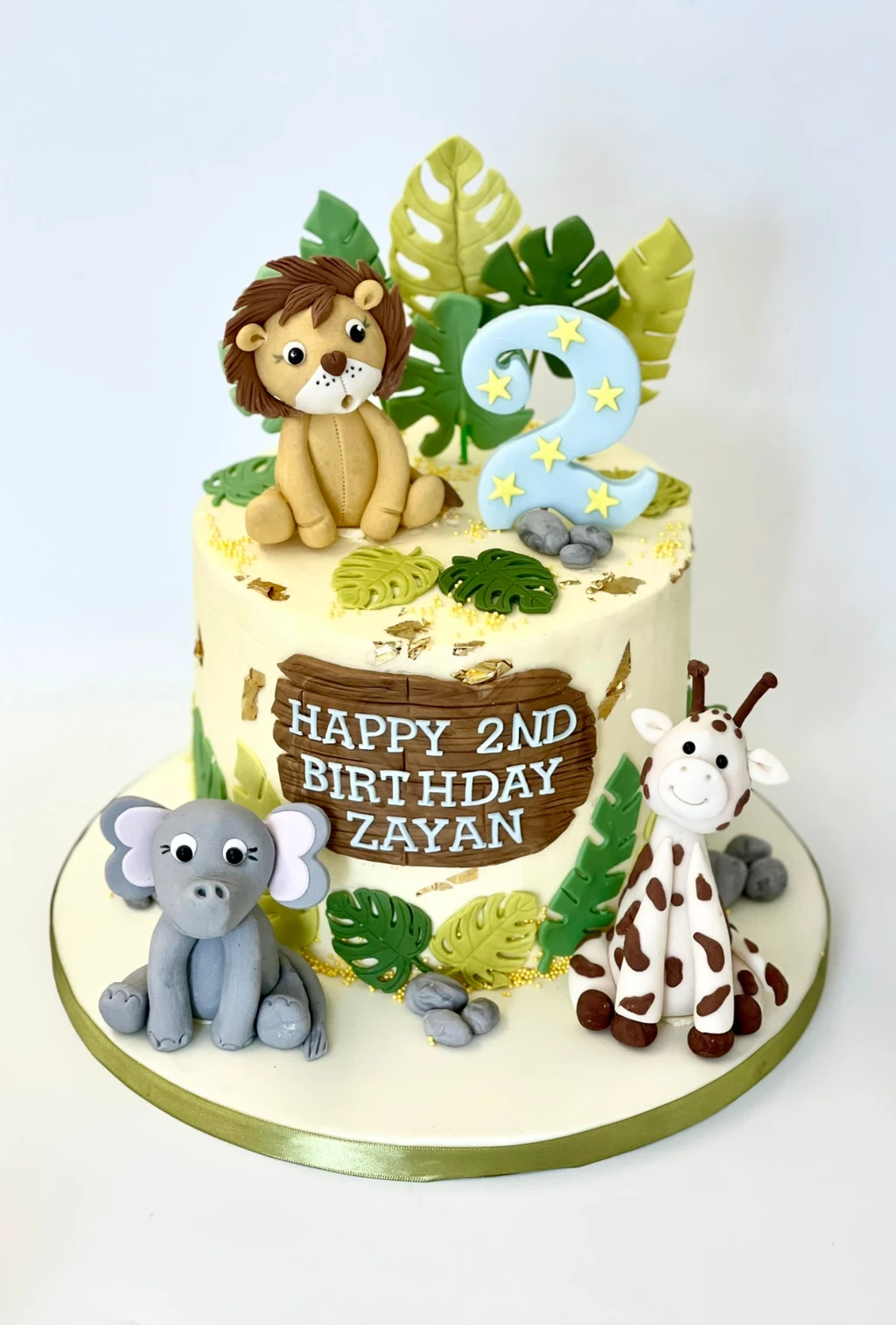 Jungle-themed second birthday cake with lion, elephant and giraffe figures and green leaves