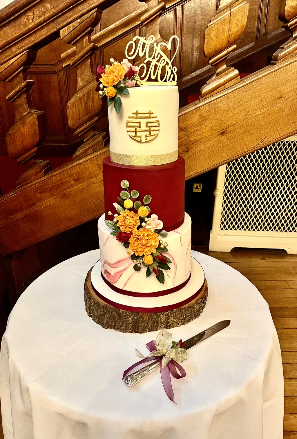 Three-tier red and ivory cake with gold lettering and bright flowers