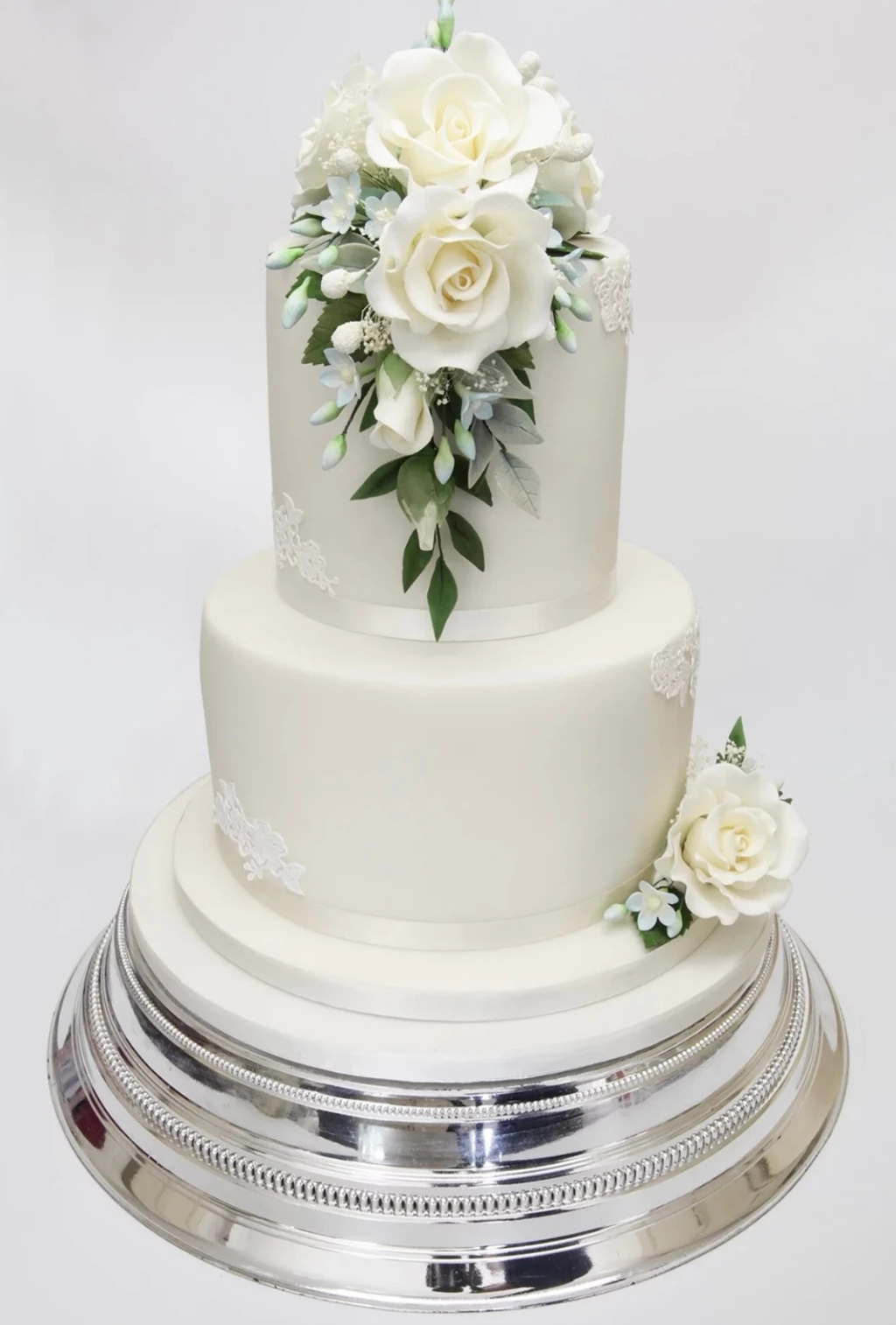 Three-tier white cake with white roses and green leaves