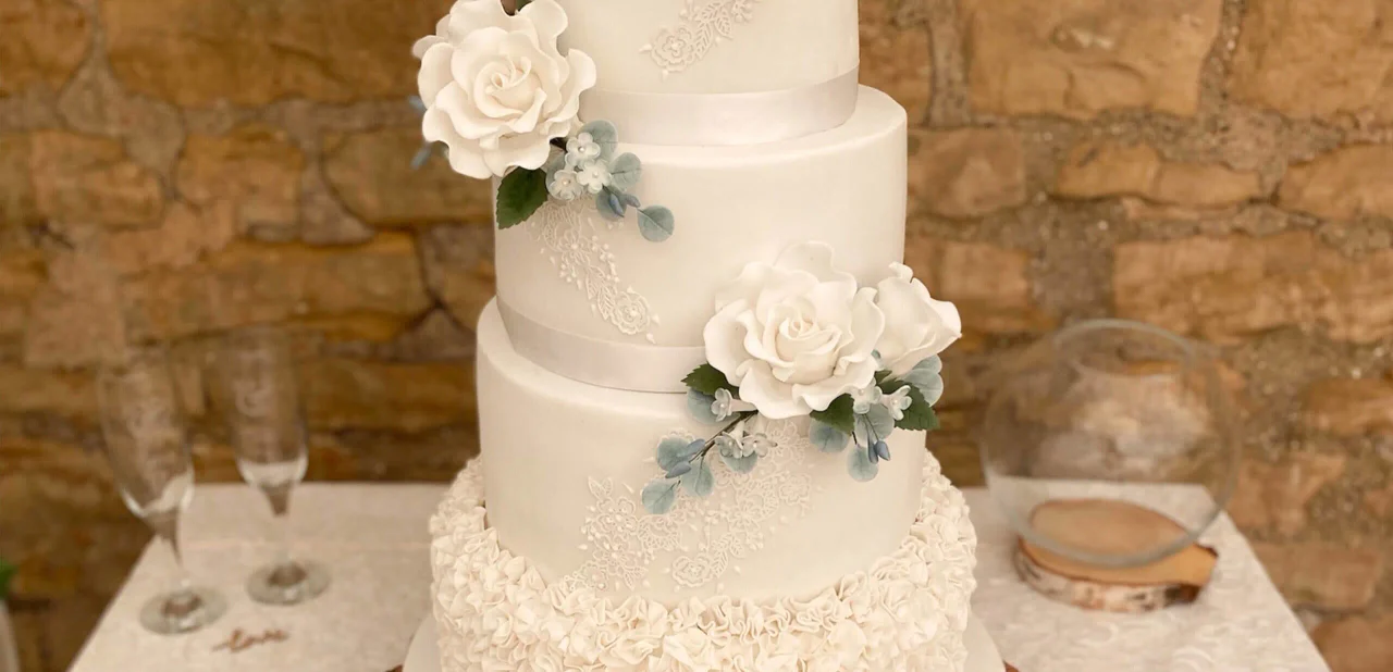 White wedding cake with sugar roses, lace details and pale green foliage