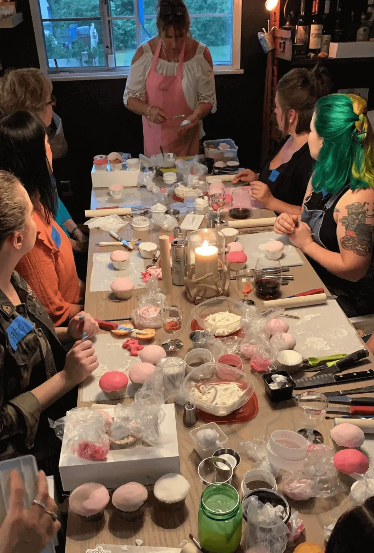 Anne demonstrating cupcake decorating to a group around a table