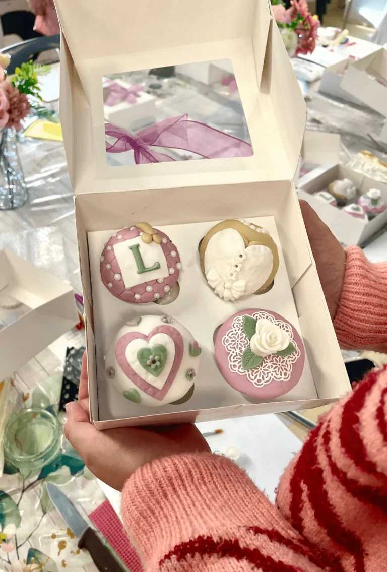 A box of four cupcakes decorated with pale pink, green and white icing